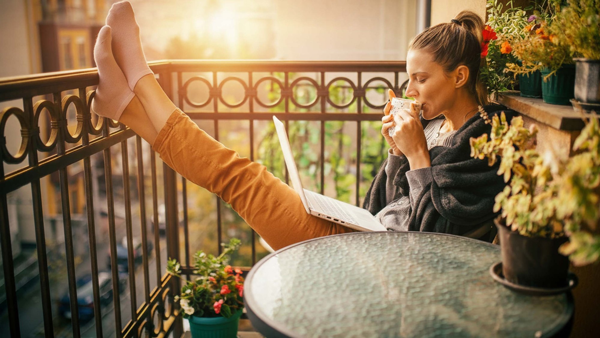 woman-balcony-sun-laptop-hero-16-9-2560x1440px